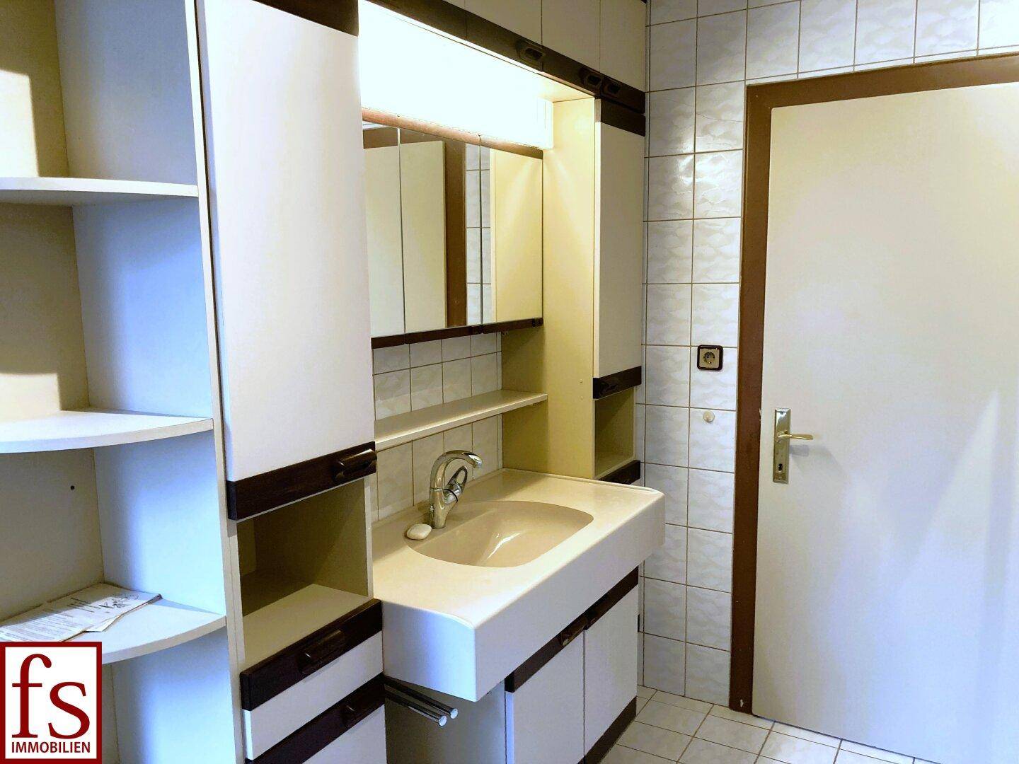 Badezimmer mit Waschtisch, Spiegelschrank und Fliesen an Wänden und Boden.