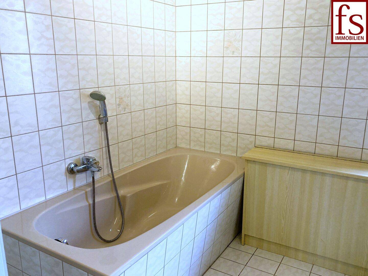 Badezimmer mit Badewanne und hellen Fliesen an den Wänden, in gutem Zustand.