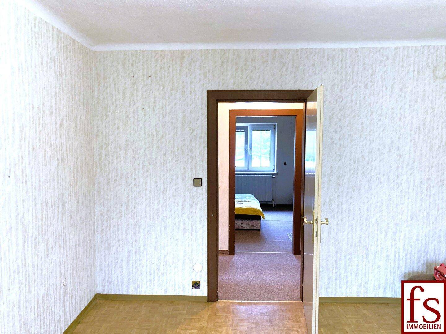 Innenraum mit Parkettboden und einer Tür, die zu einem weiteren Zimmer führt.