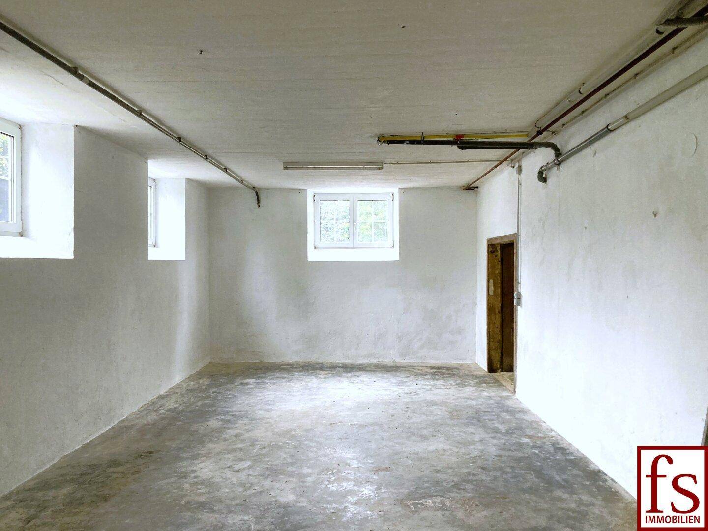 Geräumiger Kellerraum mit Betonboden und kleinen Fenstern, ideal als Lagerfläche.