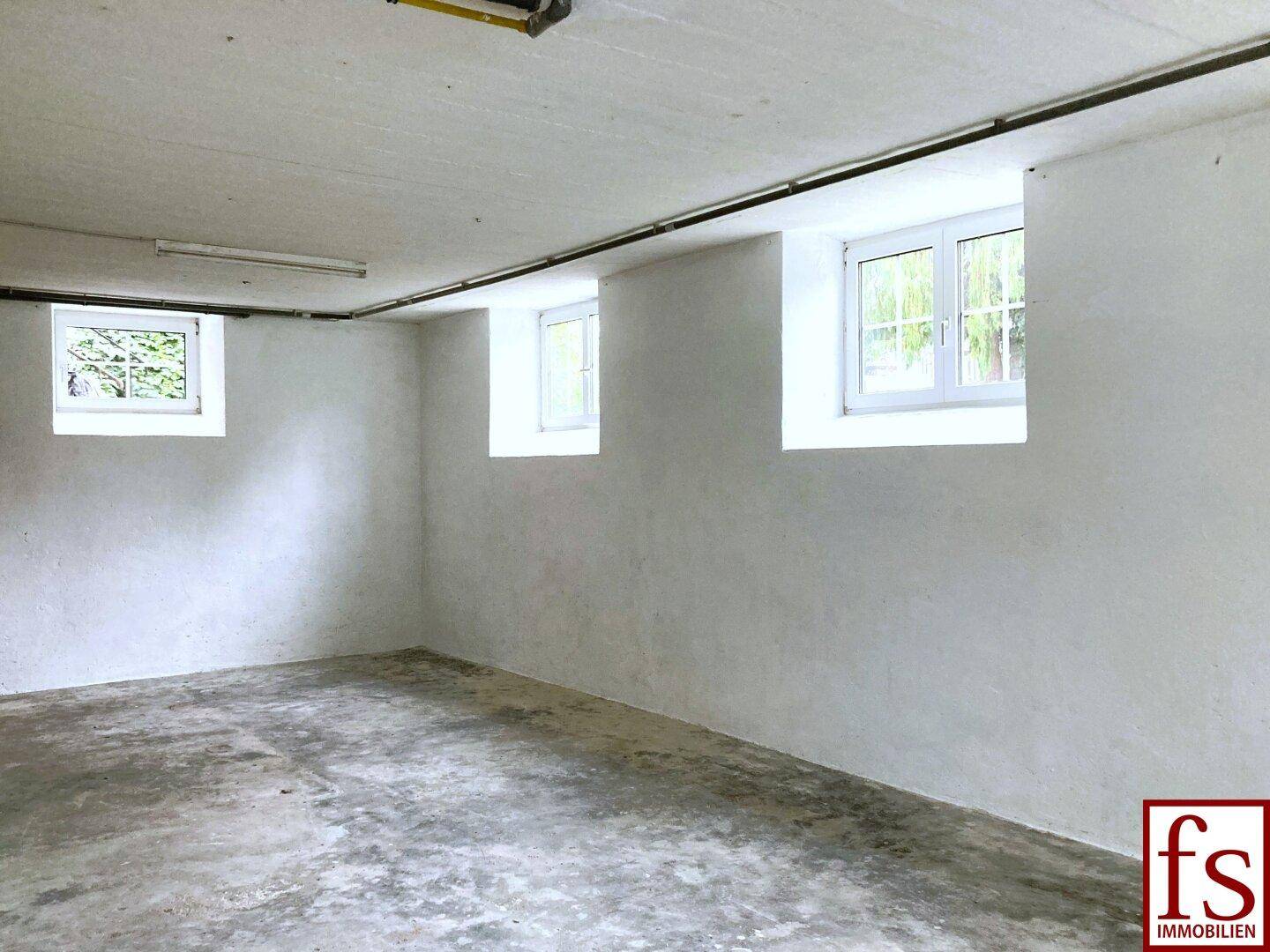 Kellerraum mit Betonboden und mehreren Fenstern, die für Belüftung sorgen.