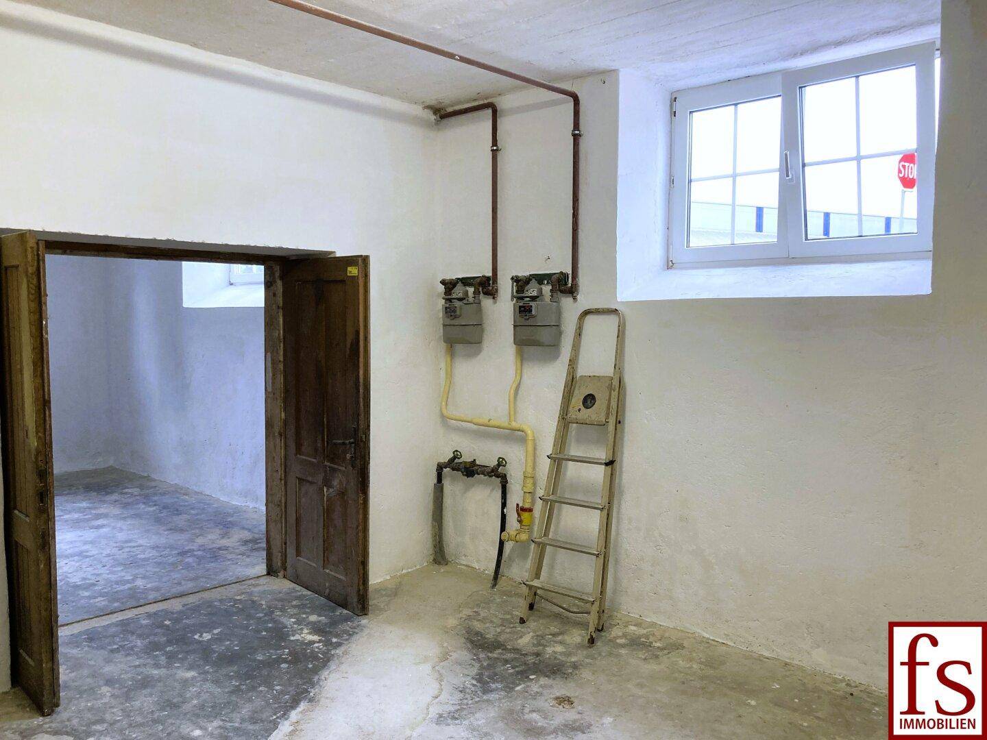 Kellerraum mit Gaszählern, Betonboden und Holztüren, bereit für die Nutzung.