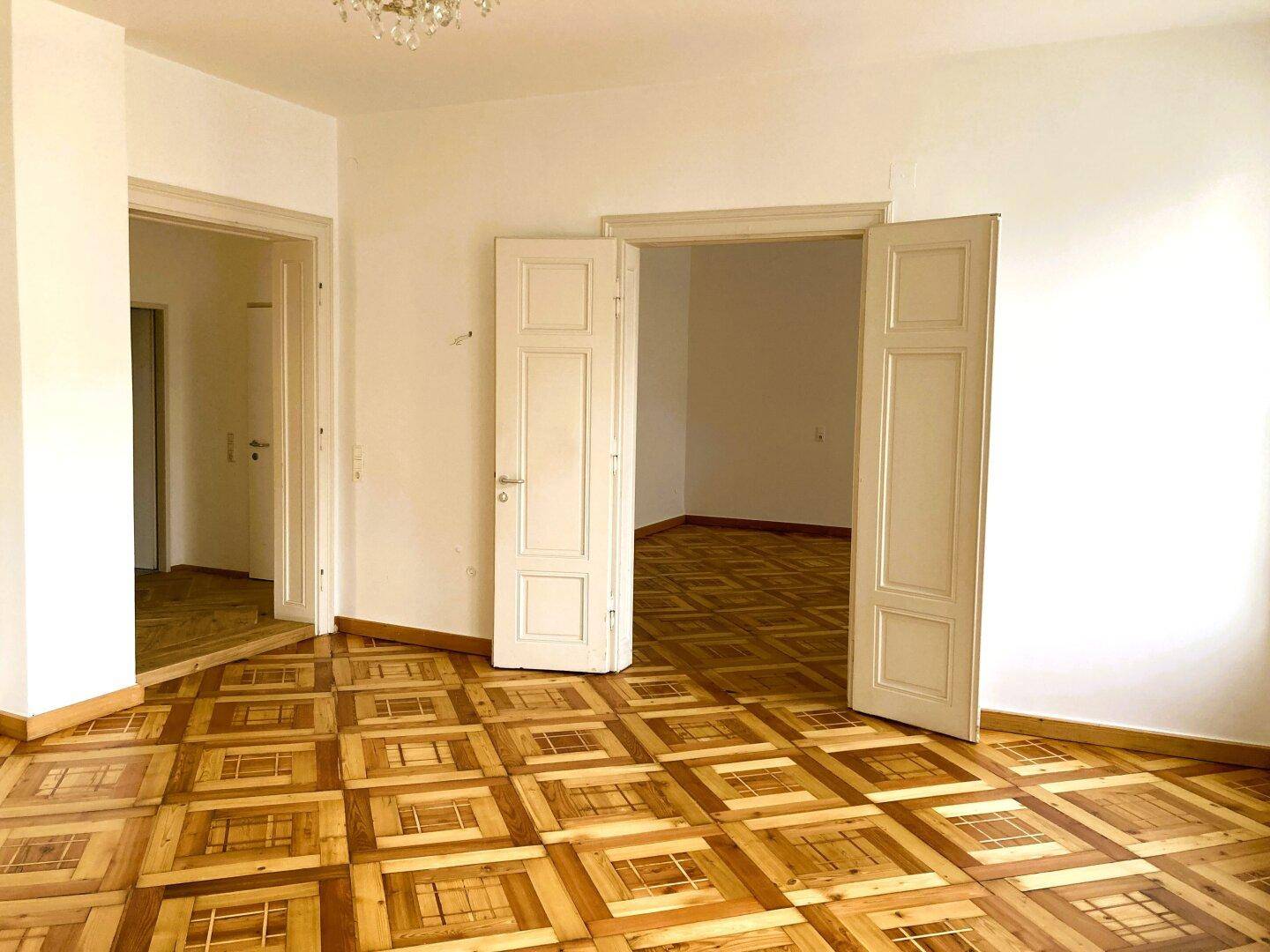 Geräumiges Zimmer mit charakteristischem Parkettboden und hohen Flügeltüren zu weiteren Räumen.