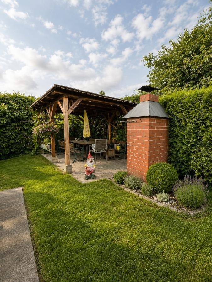 Gemütlicher Gartenbereich mit Grillplatz, Holzpergola und Gartenmöbeln, umgeben von Hecken.