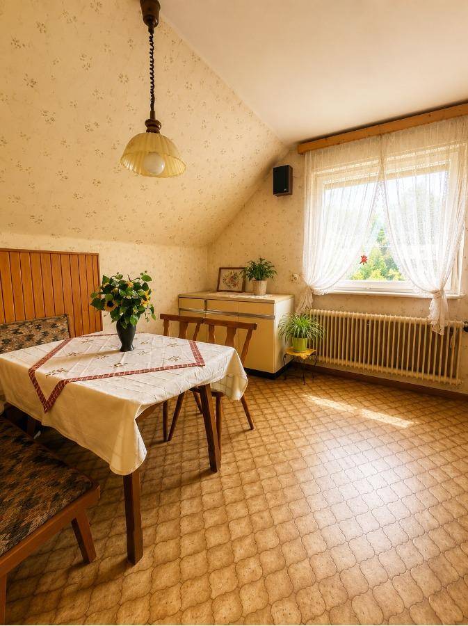 Esszimmer im Dachgeschoss mit gemusterter Tapete, Vinylboden und Blick ins Grüne durch das Fenster.
