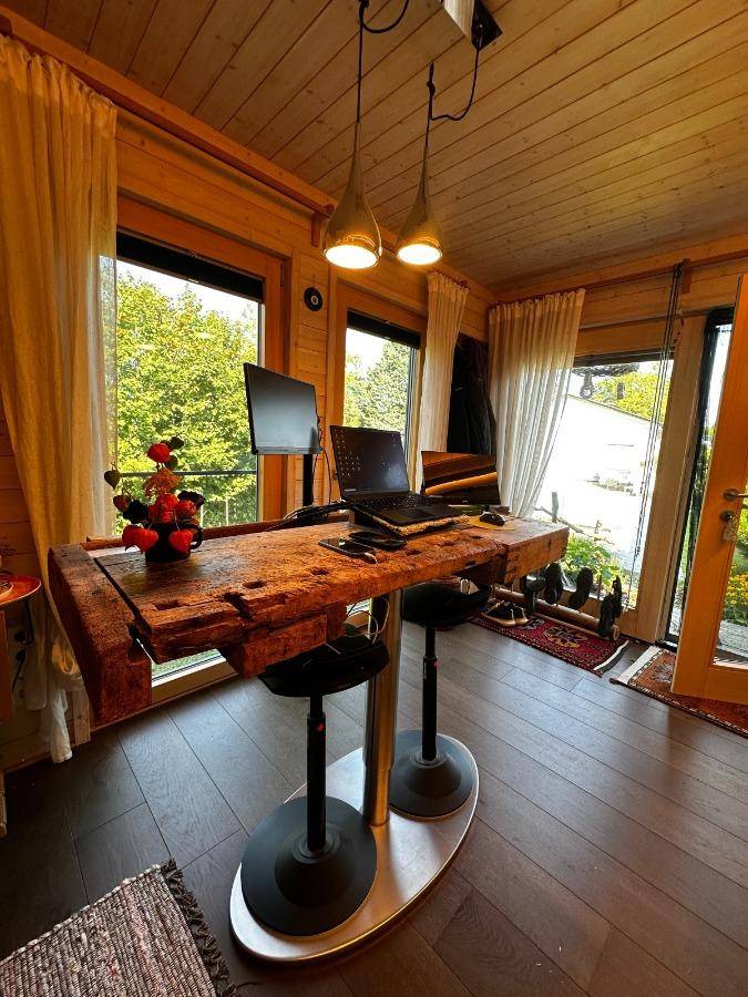 Helles Büro mit rustikalem Holztisch, großen Fenstern und Blick ins Grüne.