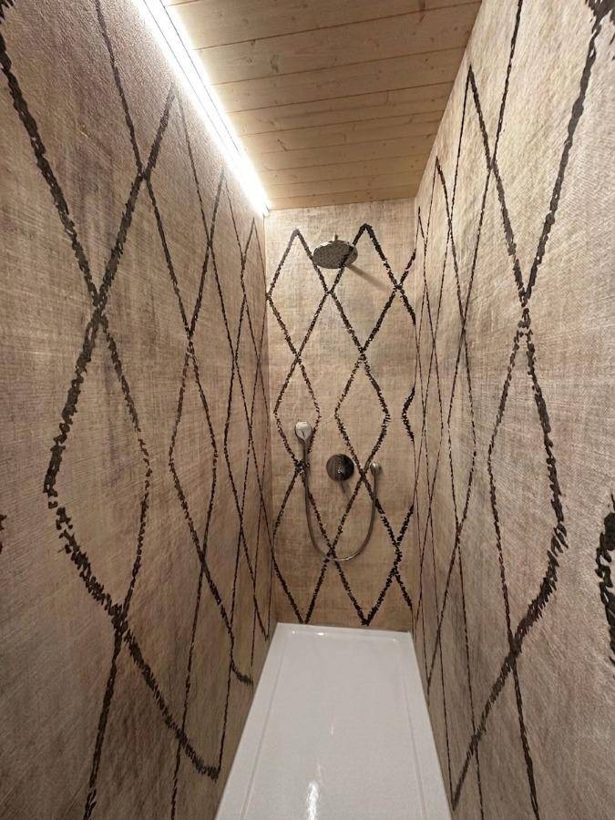 Moderne Duschkabine mit gemusterten Wänden und Regendusche in einem kompakten Badezimmer.