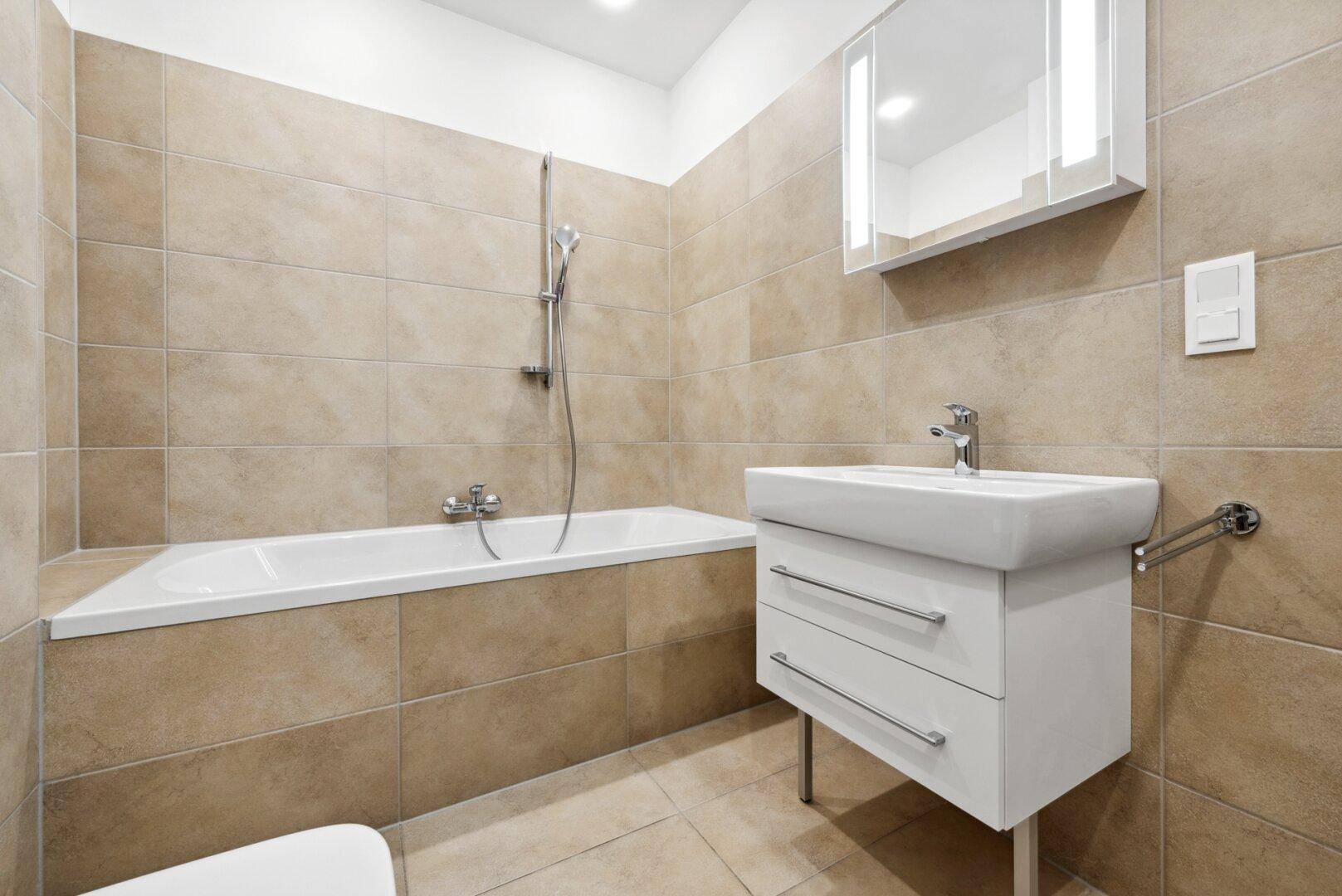 Modernes Badezimmer mit beigefarbenen Fliesen, Badewanne und einem Waschbecken mit Spiegelschrank.