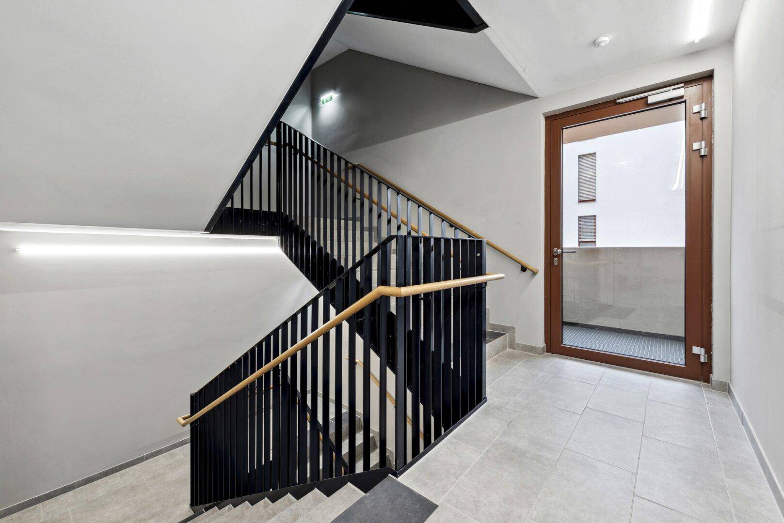 Modernes Treppenhaus mit schwarzem Geländer und Holzhandlauf, das zu den oberen Etagen führt.