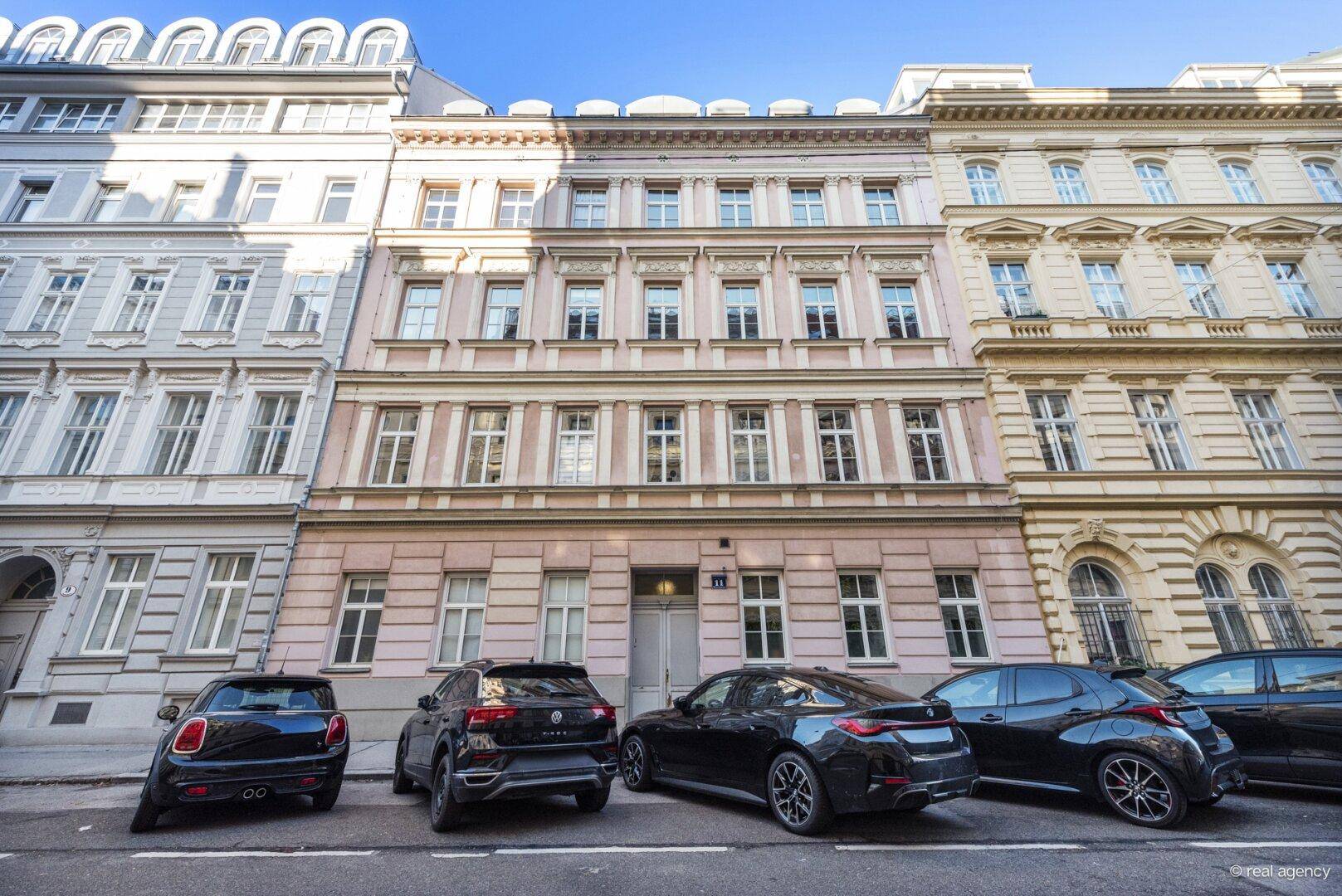 Klassische Fassade eines Stadthauses mit vielen Fenstern und geparkten Autos davor.