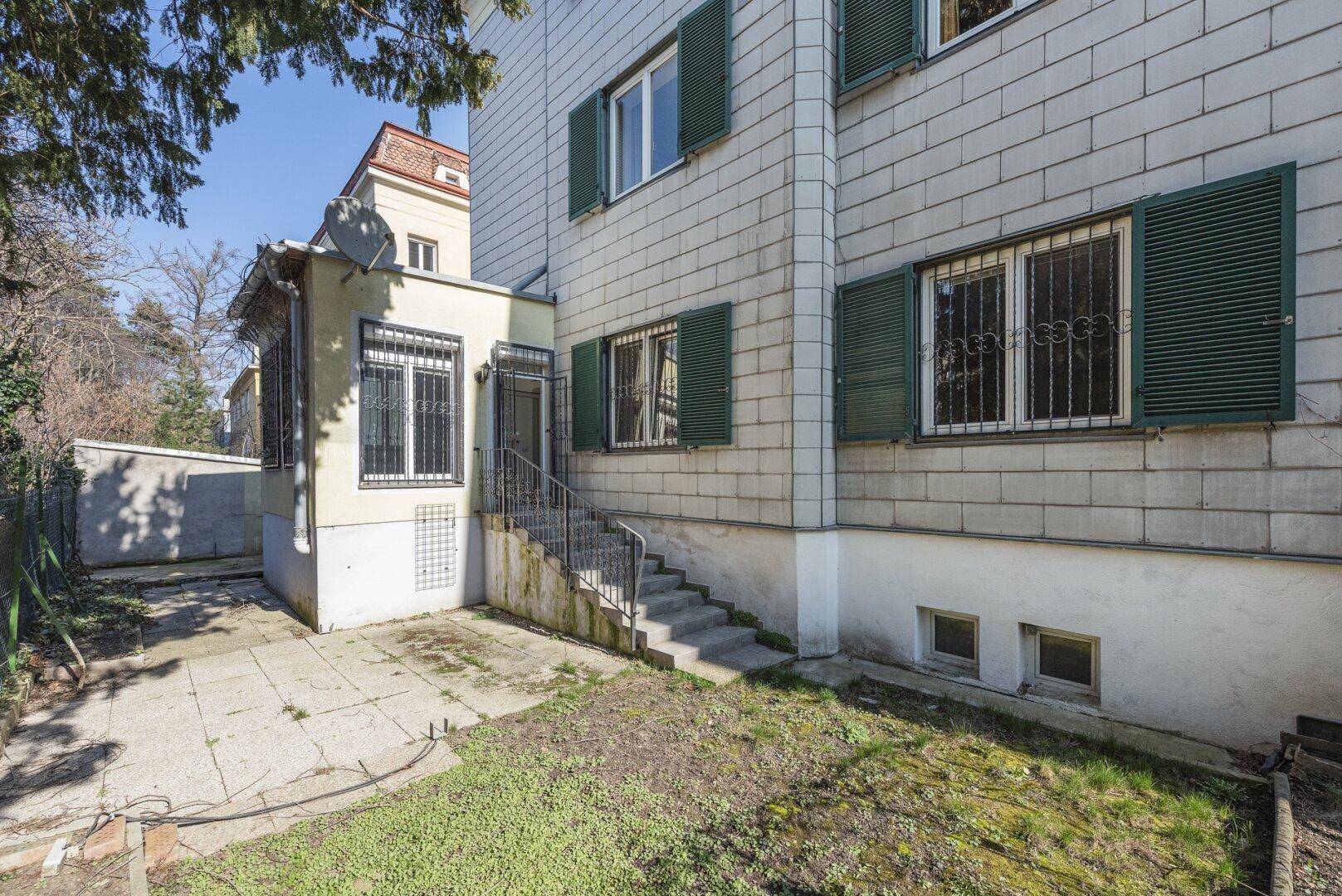 Außenansicht des Gebäudes mit grünen Fensterläden und einem unmöblierten Gartenbereich.