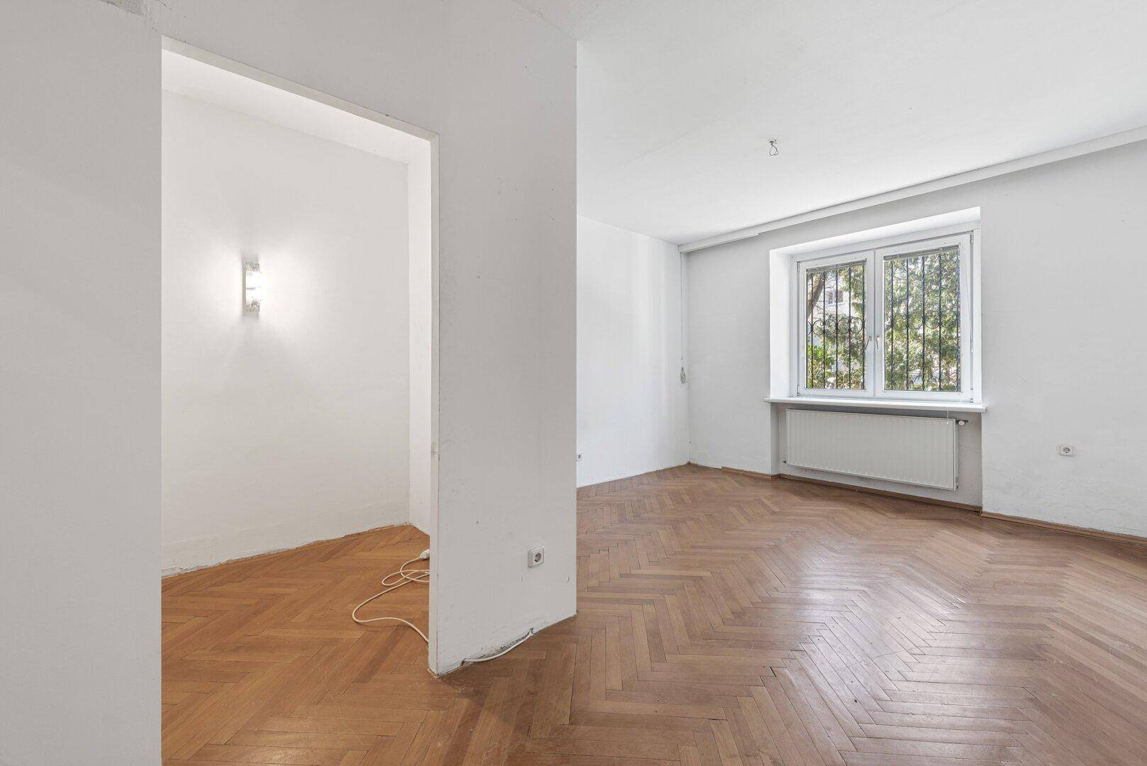 Leeres Schlafzimmer mit Fischgrätparkett und vorbereitetem Bereich für einen begehbaren Kleiderschrank.