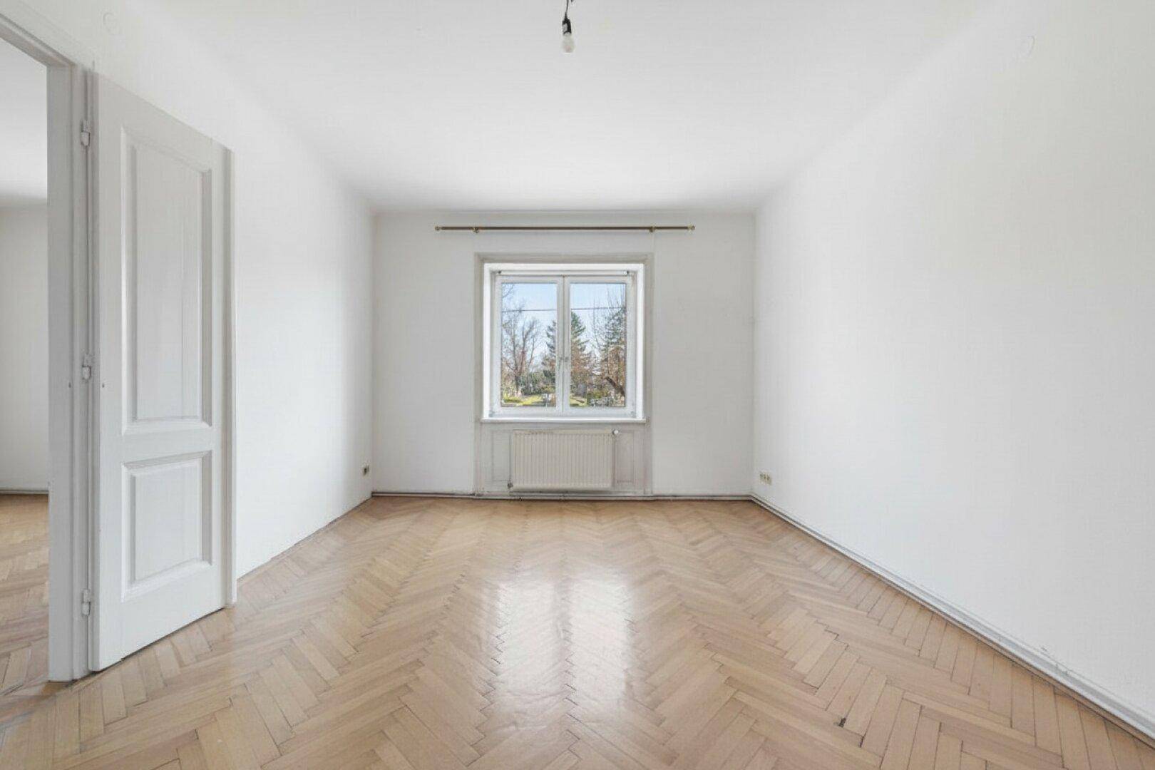 Leeres, helles Wohnzimmer mit Fischgrätparkett und großem Fenster.