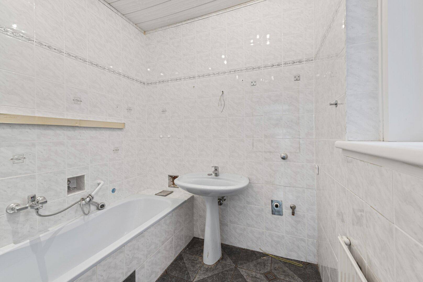 Badezimmer mit Badewanne, Waschbecken und weißen Fliesen an den Wänden.