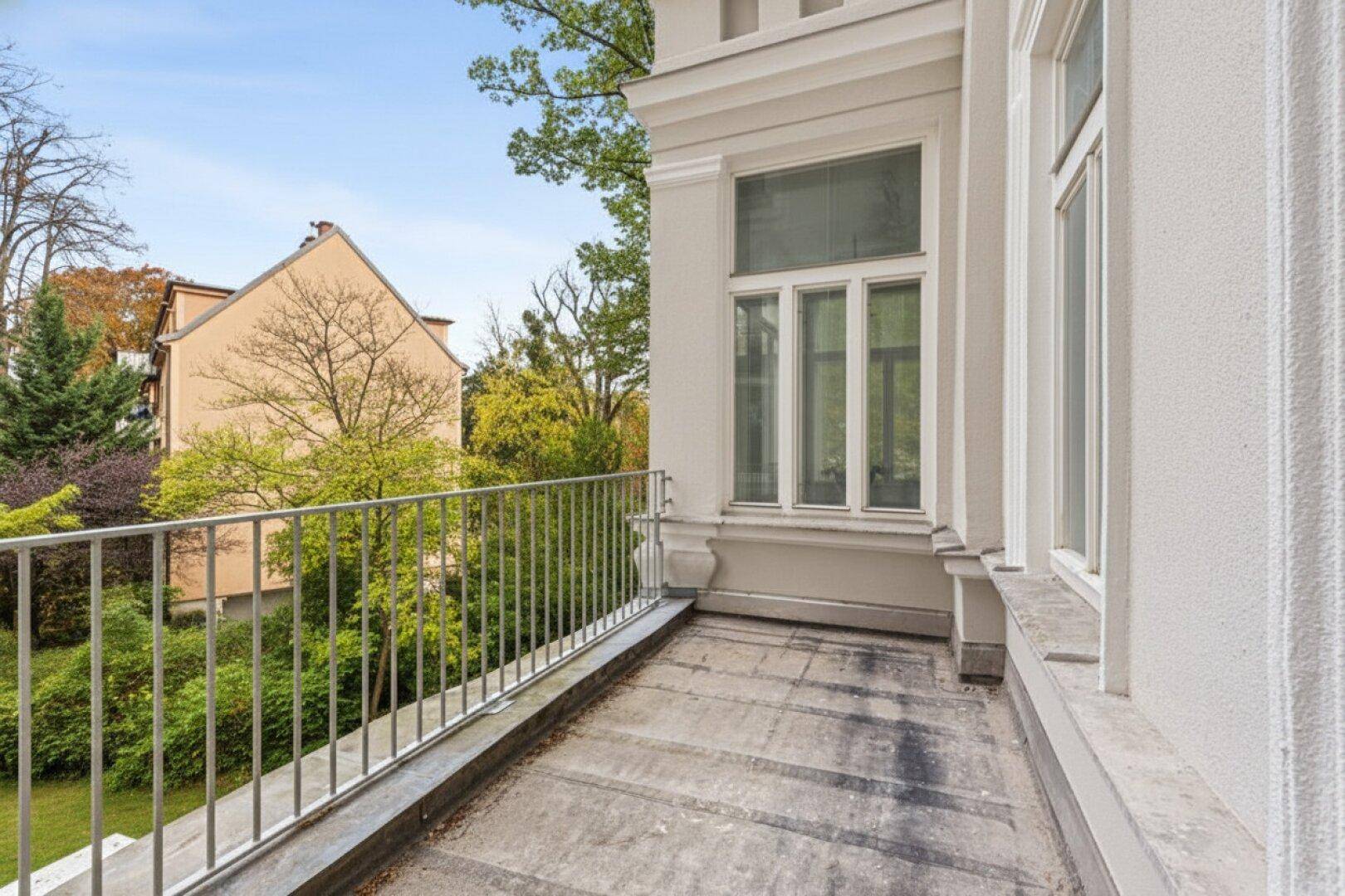Geräumiger Balkon mit Metallgeländer und weitem Blick ins Grüne sowie auf benachbarte Gebäude.