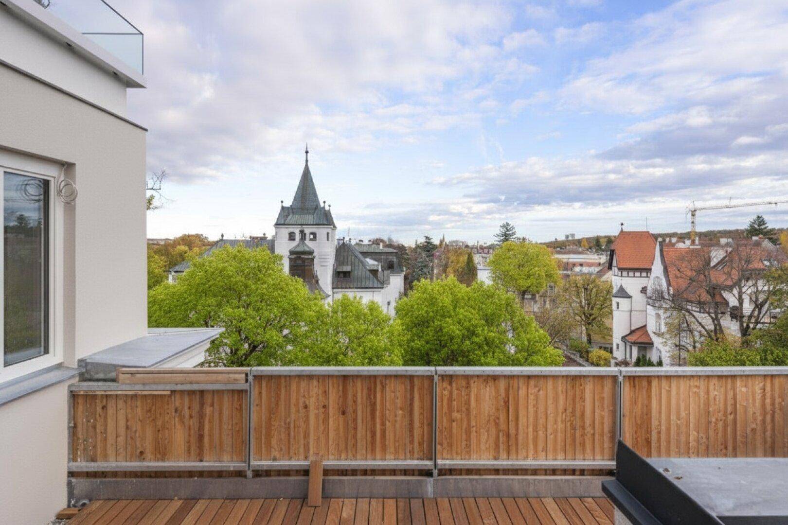 Geräumige Dachterrasse mit Holzbelag und Panoramablick über die Stadt mit historischen Gebäuden und viel Grün.