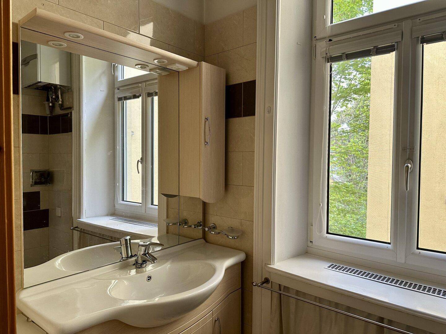 Helles Badezimmer mit Fenster, Waschbecken und Spiegelschrank, in gutem Zustand.