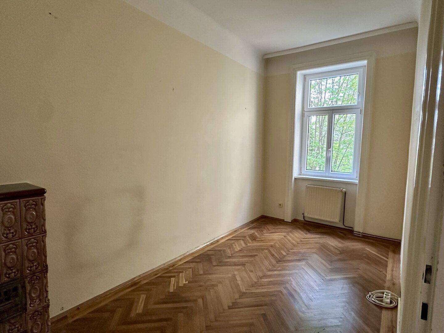 Heller Raum mit Fischgrätparkett und einem traditionellen Kachelofen, ideal als Schlaf- oder Arbeitszimmer.