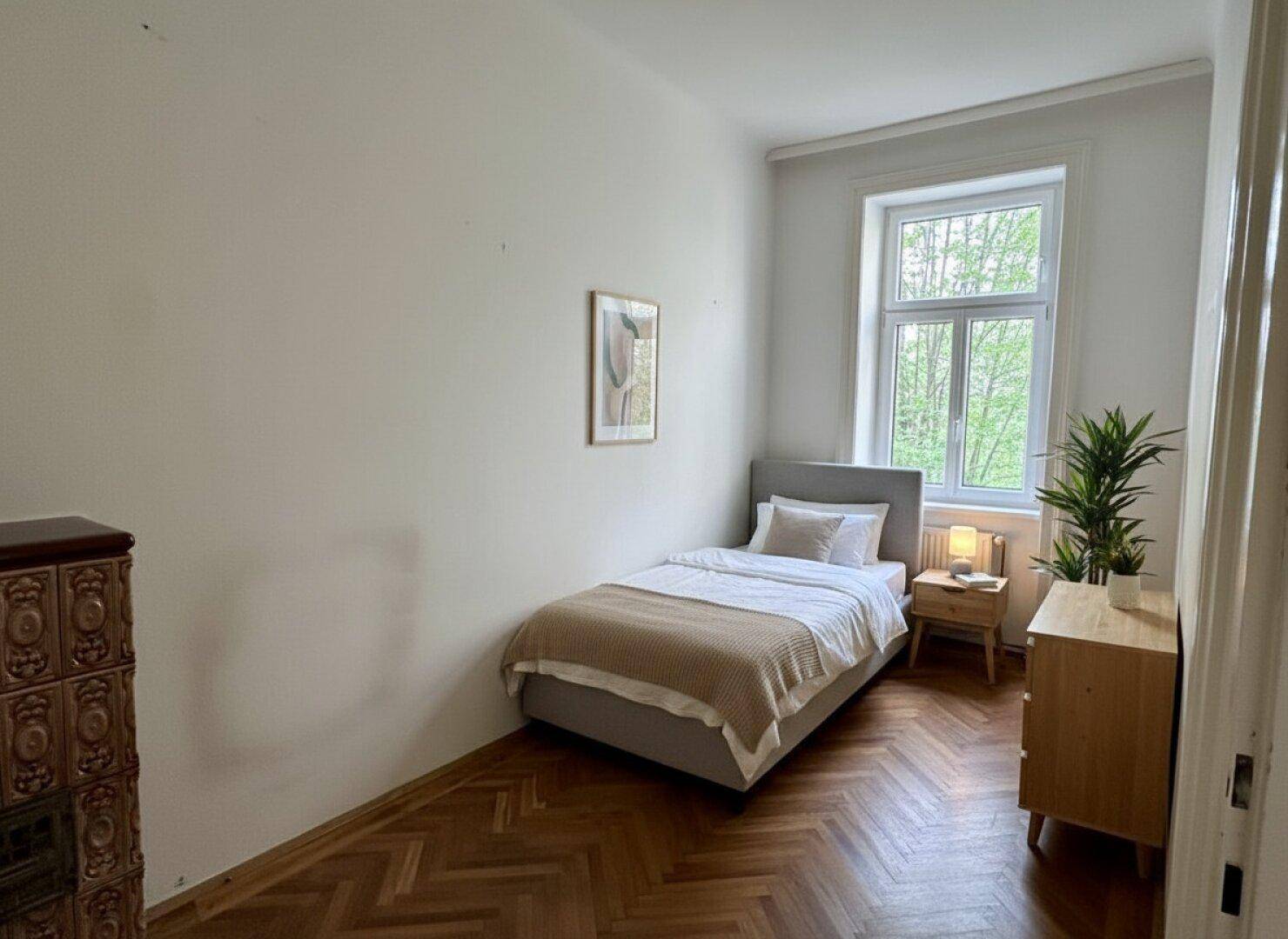 Gemütliches Schlafzimmer mit Einzelbett, Fischgrätparkett und einem traditionellen Kachelofen.