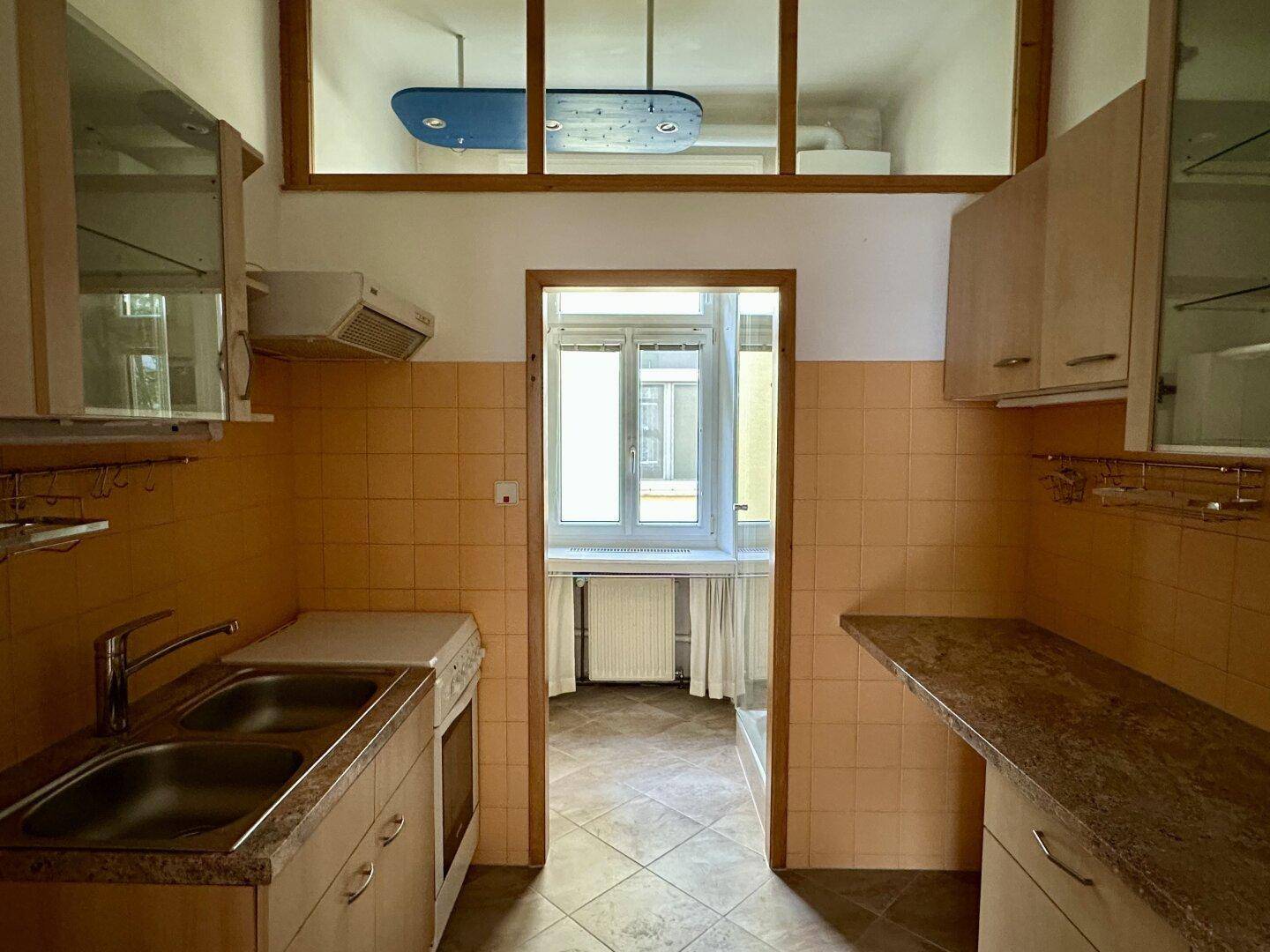 Ältere Küche mit orangefarbenen Fliesen, Holzschränken und Blick auf den Innenhof.