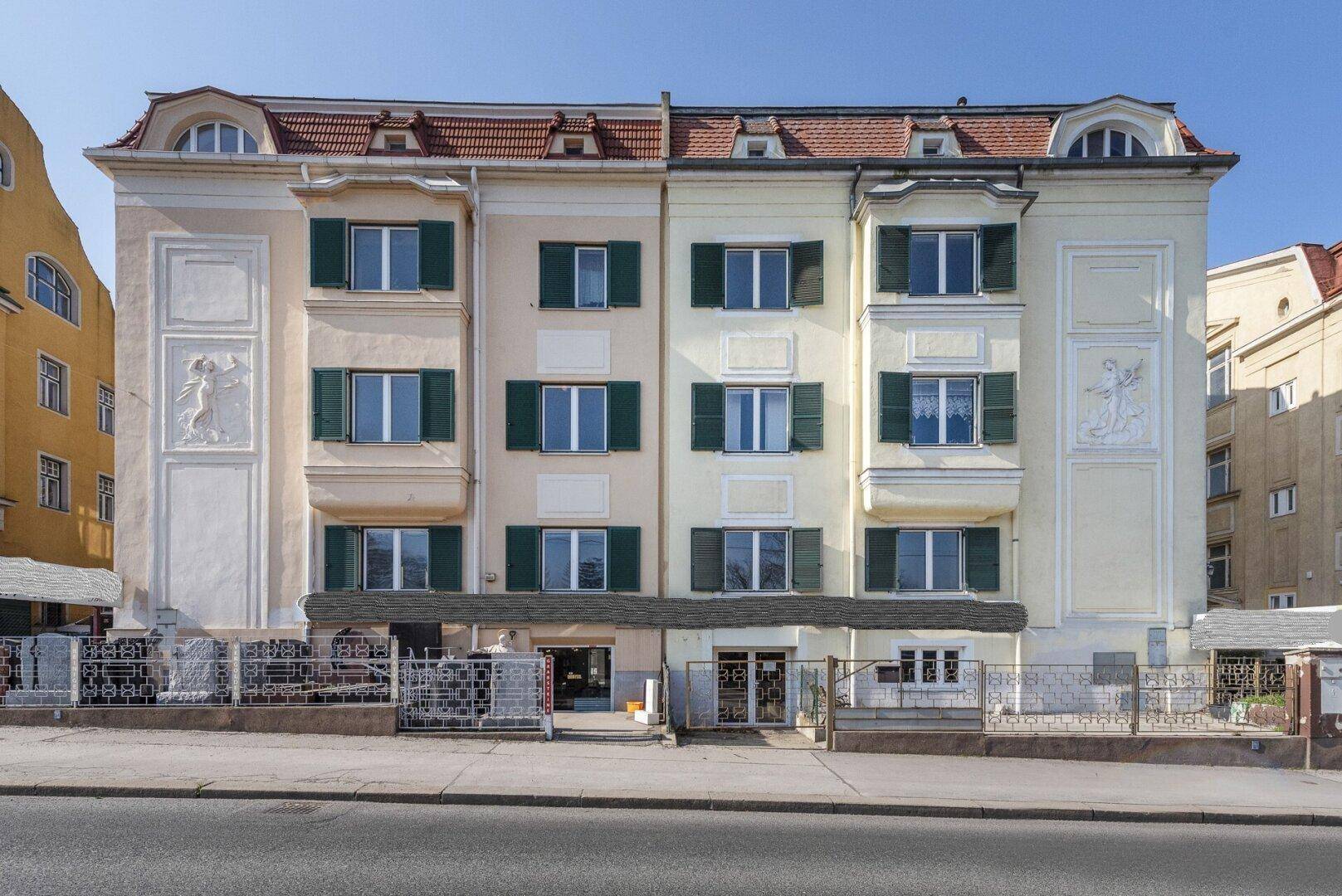 Mehrstöckiges Gebäude mit klassischer Fassade, verzierten Elementen und grünen Fensterläden.