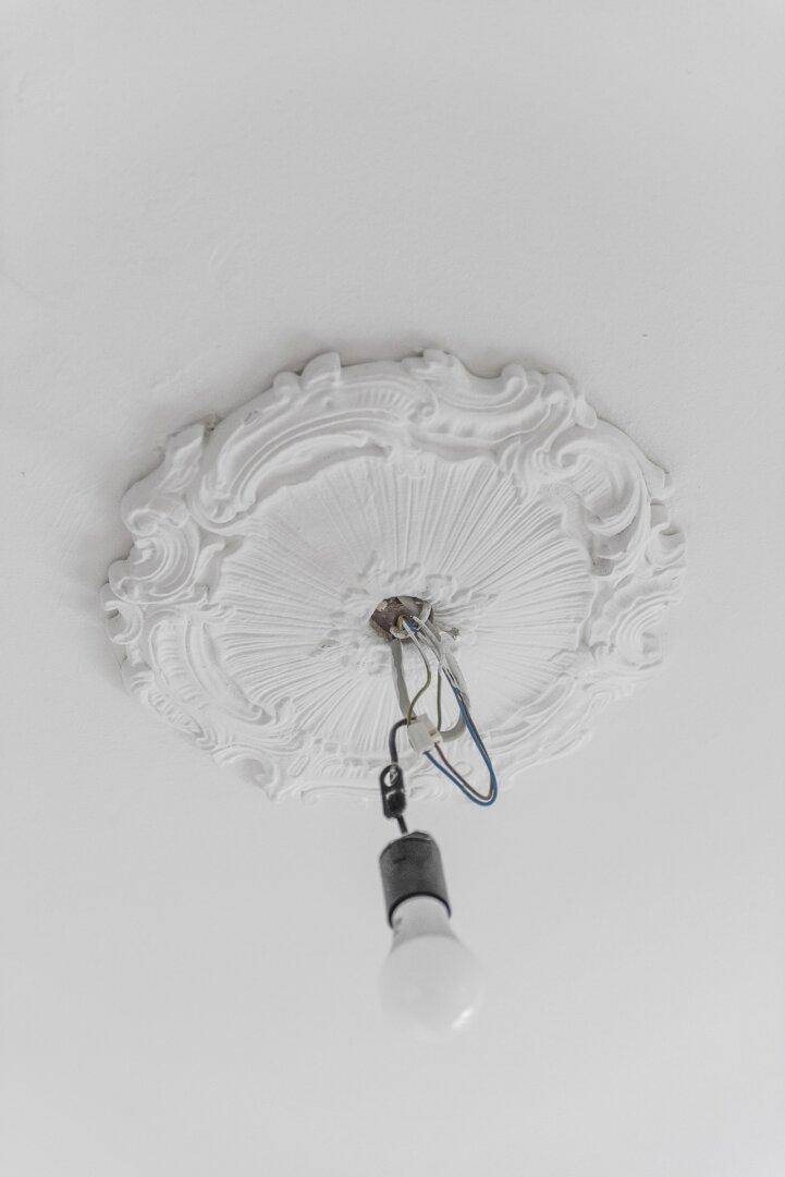 Weiße Stuckrosette an der Decke mit freiliegenden Kabeln für eine zukünftige Beleuchtung.