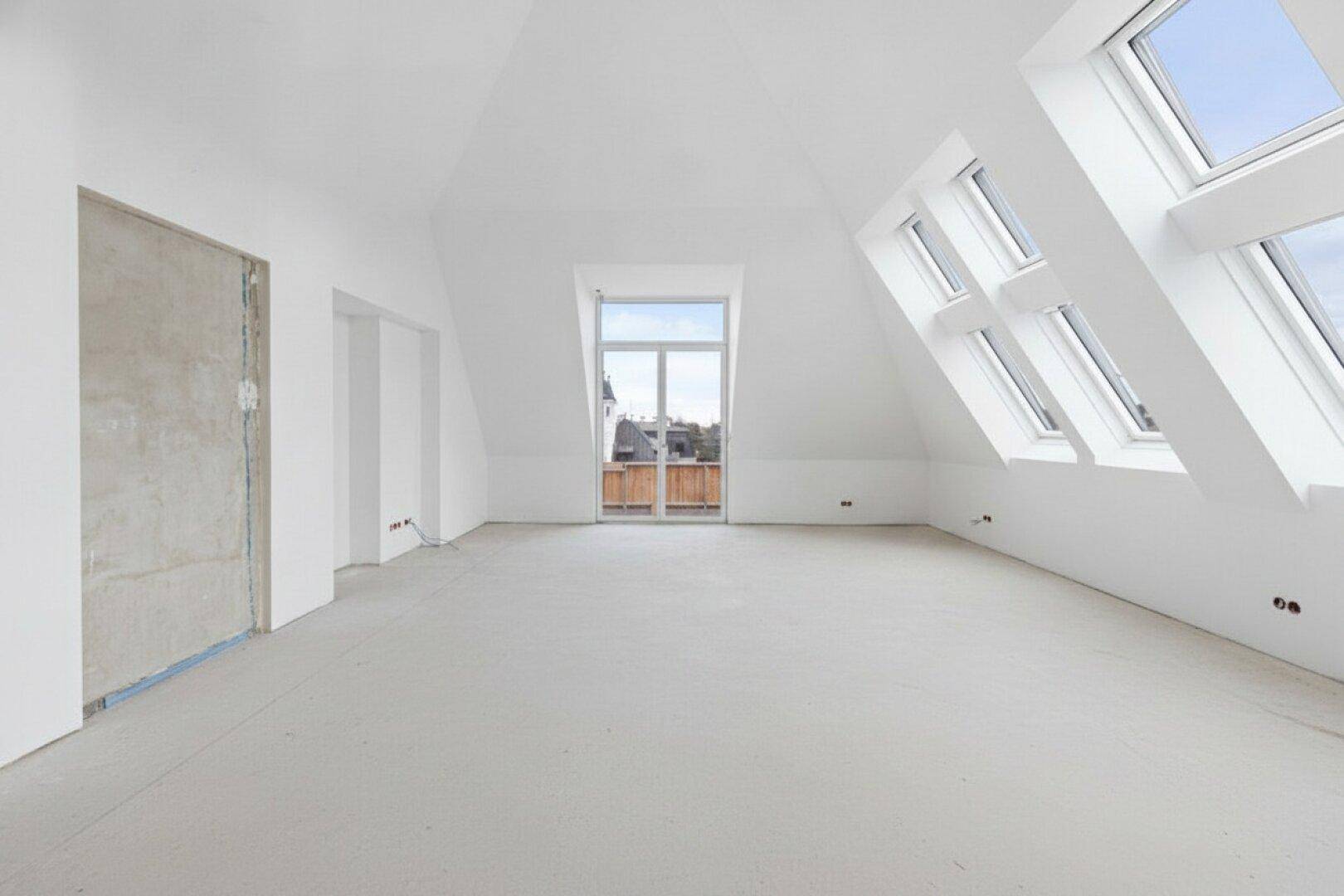 Leerer Raum im Dachgeschoss mit schrägen Wänden, Dachfenstern und Zugang zu einem kleinen Balkon.