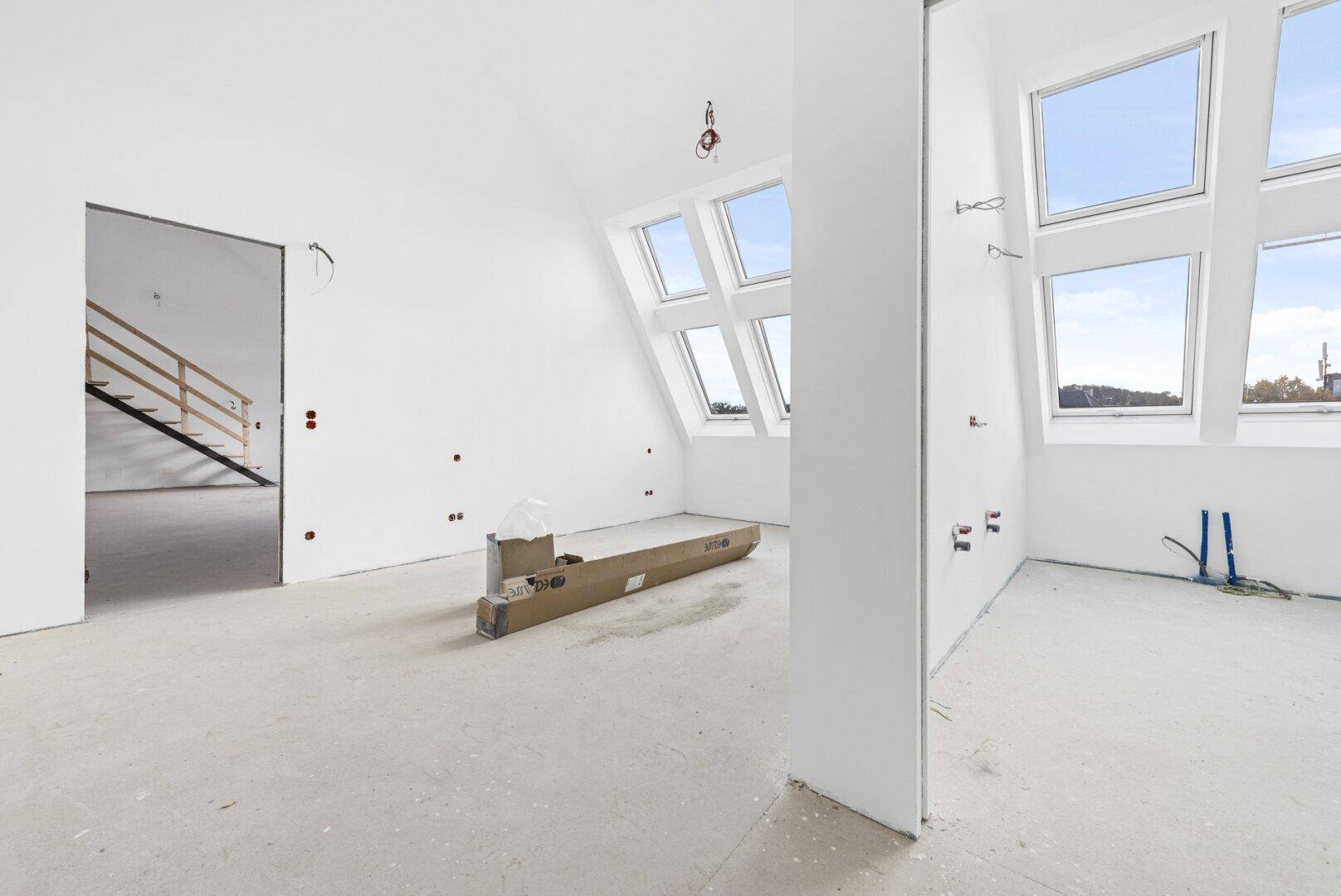 Unfertiger Innenraum mit großen Dachfenstern und Blick auf die Umgebung, bereit für den Ausbau.