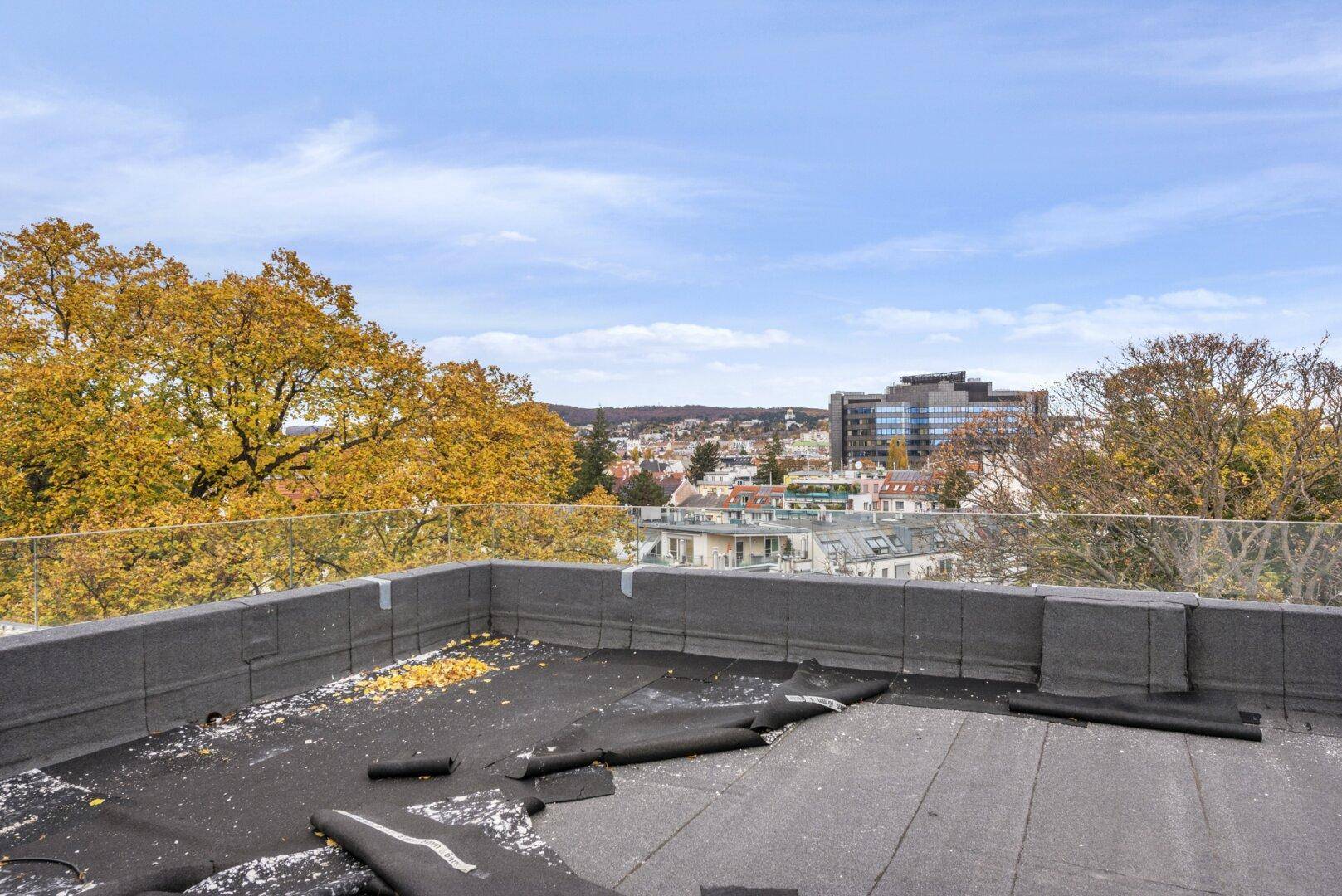 Unfertige Dachfläche mit Baumaterialien und Panoramablick über die Stadt und umliegende Natur.