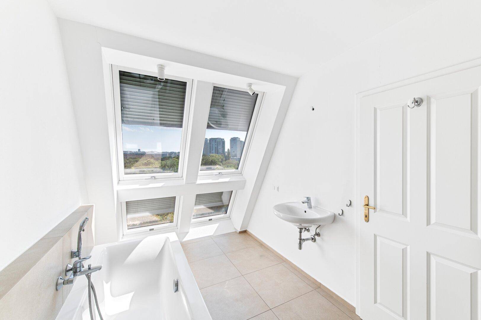 Modernes Badezimmer mit Badewanne, Waschbecken und Dachfenstern, die viel Licht hereinlassen.