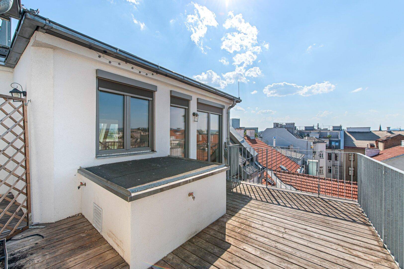 Geräumige Dachterrasse mit Holzboden und Blick über die Dächer der Stadt.
