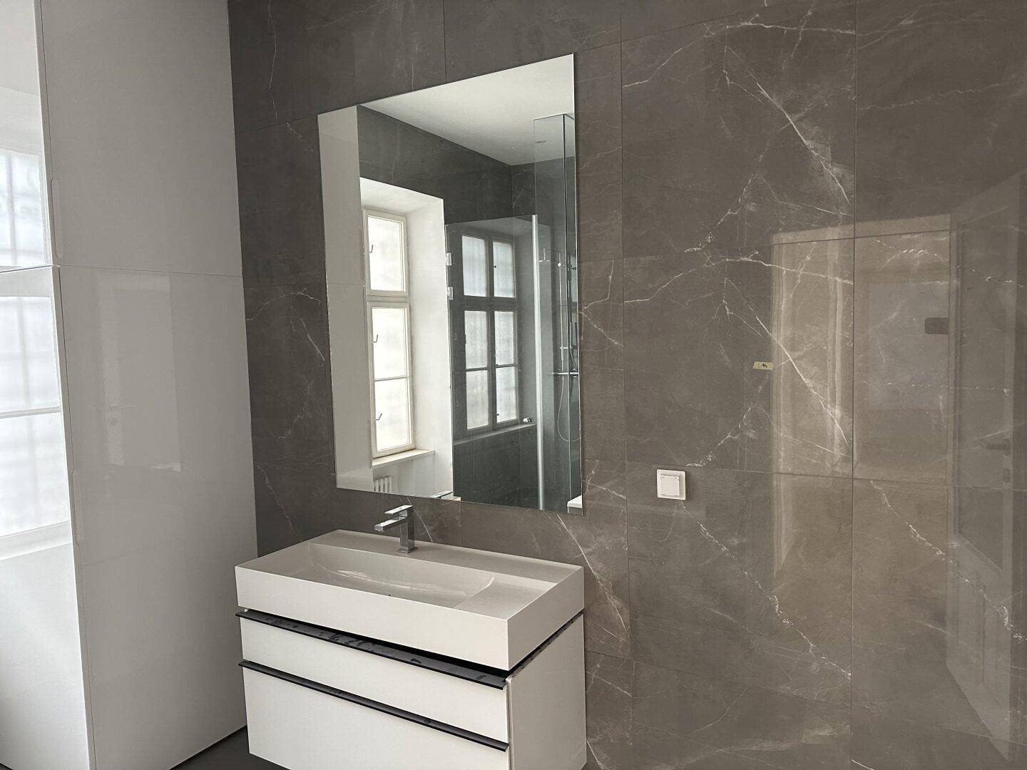 Modernes Badezimmer mit grauen Marmorfliesen, einem Waschtisch mit Unterschrank und einem großen Spiegel.