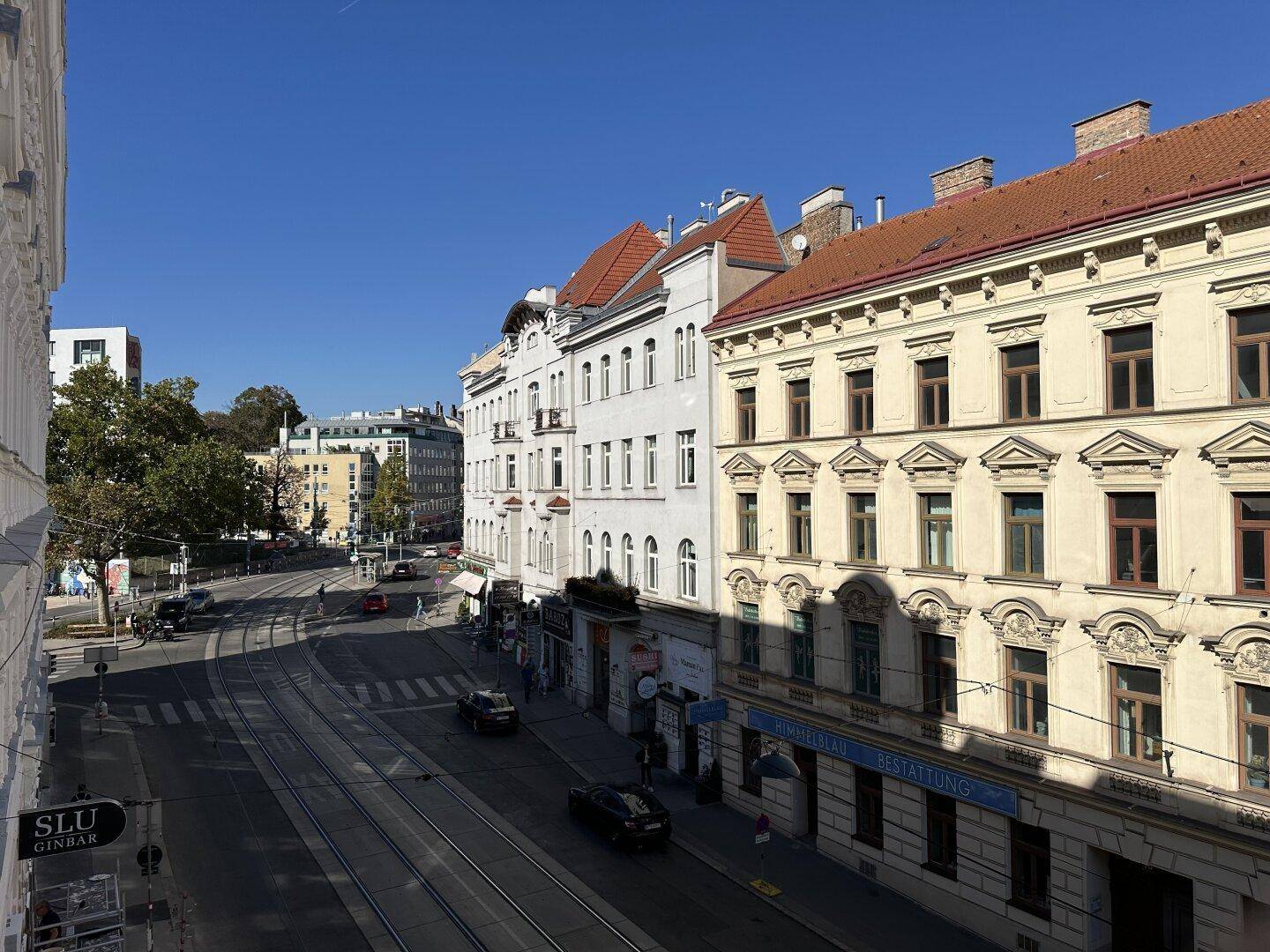 Blick von einem oberen Stockwerk auf eine belebte Straße mit Straßenbahnschienen und historischen Gebäuden.