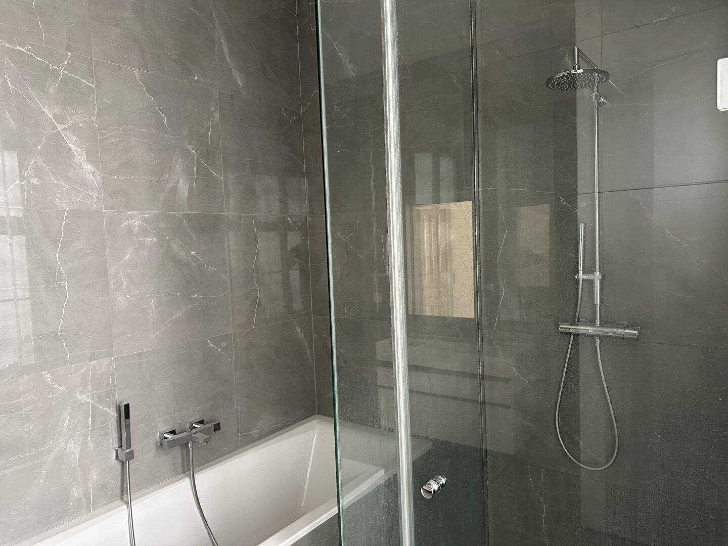 Modernes Badezimmer mit grauen Marmorfliesen, einer Regendusche und einer Badewanne hinter Glas.