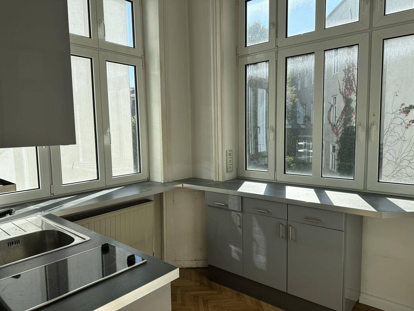 Küchenzeile mit grauen Unterschränken, Spüle, Induktionskochfeld und großen Fenstern für viel Licht.