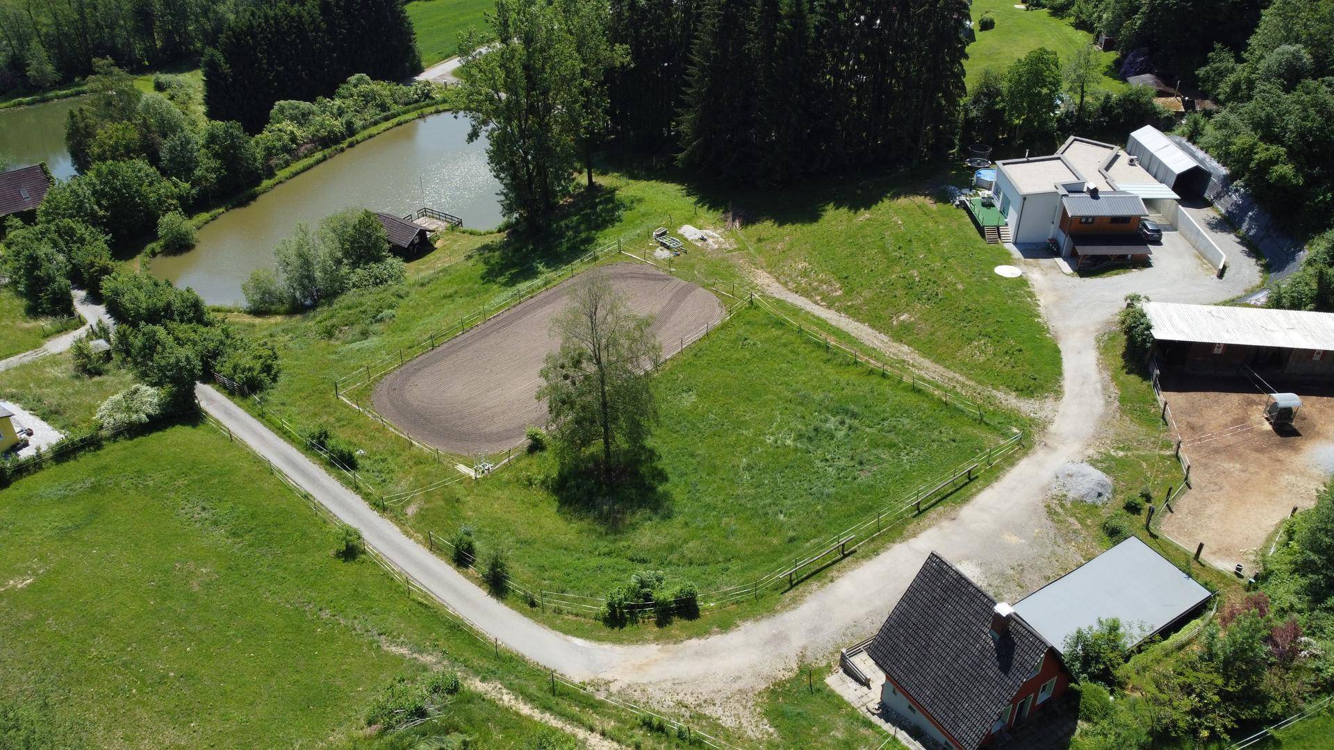 Weitläufige Luftaufnahme des Anwesens mit Gebäuden, Reitplatz, Teich und Zufahrtswegen.