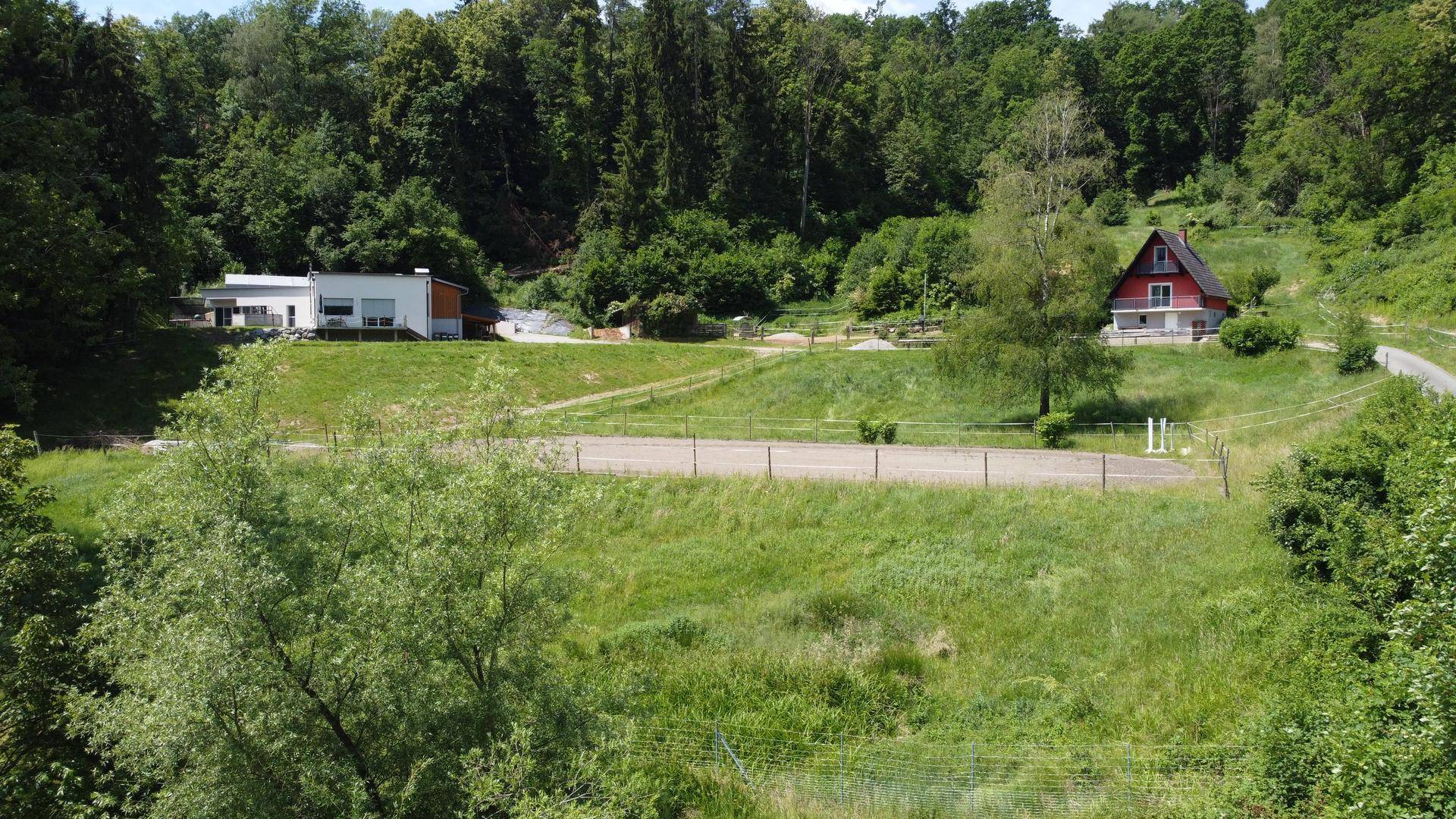 Luftaufnahme des Anwesens mit zwei Gebäuden, umgeben von grünen Hügeln und Wäldern.