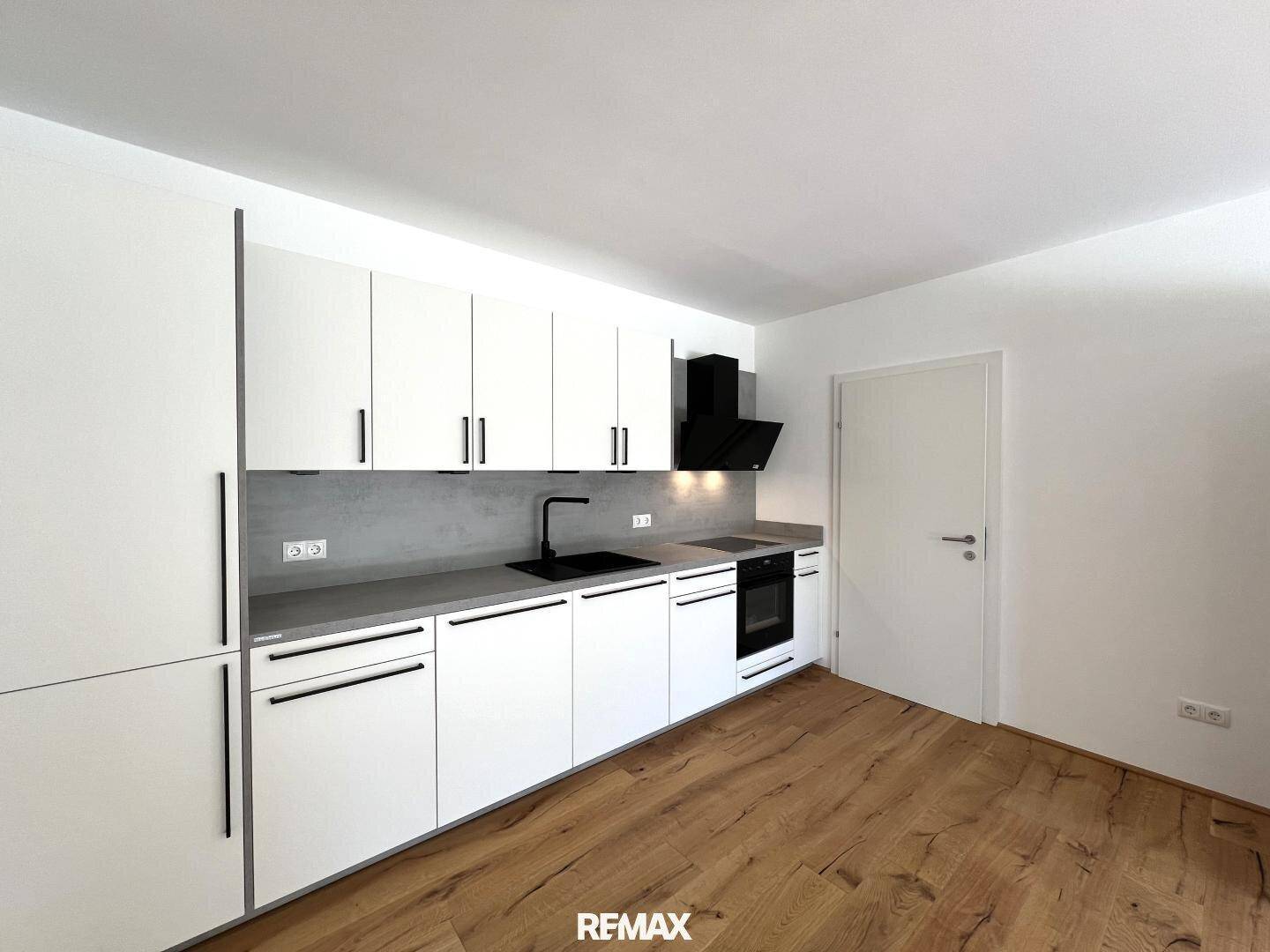 Neue, moderne Küche mit weißen Fronten, integrierten Geräten und dunkler Arbeitsplatte.