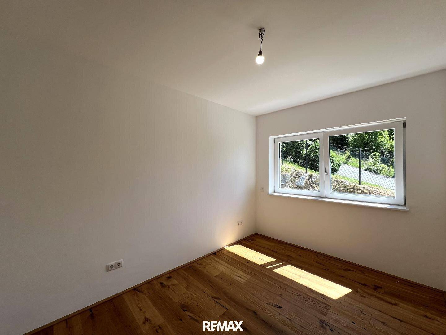 Ruhiges Schlafzimmer mit Holzboden und Fenster, das viel Tageslicht hereinlässt und einen grünen Ausblick bietet.