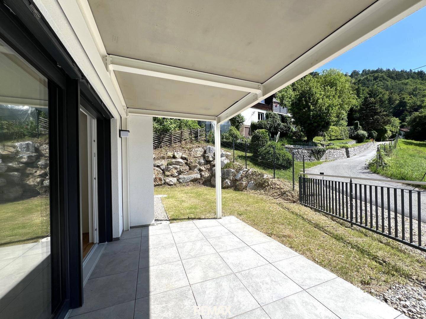 Überdachte Terrasse mit Fliesenboden und Blick auf die umliegende Natur und den Gartenbereich.
