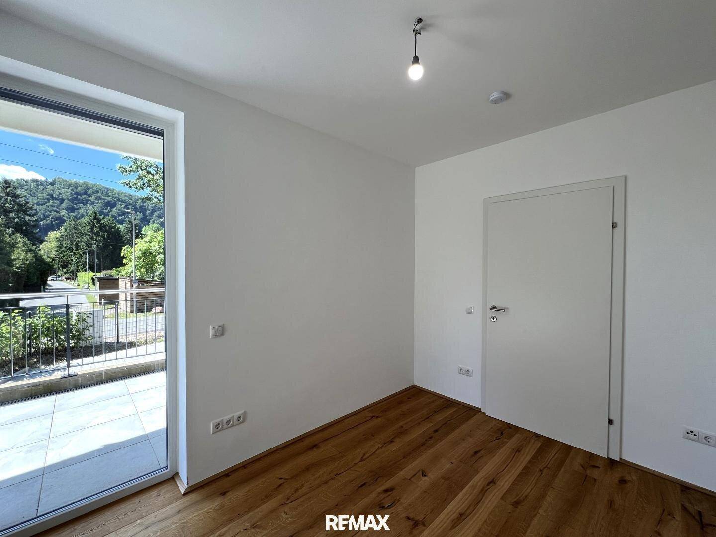 Helles Zimmer mit Holzboden und Zugang zu einem Außenbereich, ideal als Schlaf- oder Arbeitszimmer.