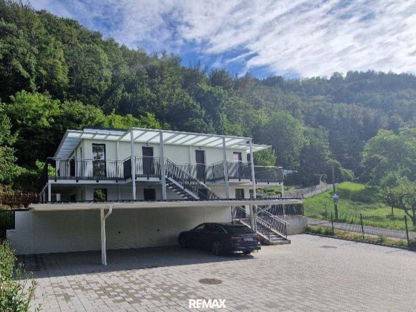 Gesamtansicht des modernen Wohnkomplexes mit Parkplätzen und umgeben von bewaldeten Hügeln.