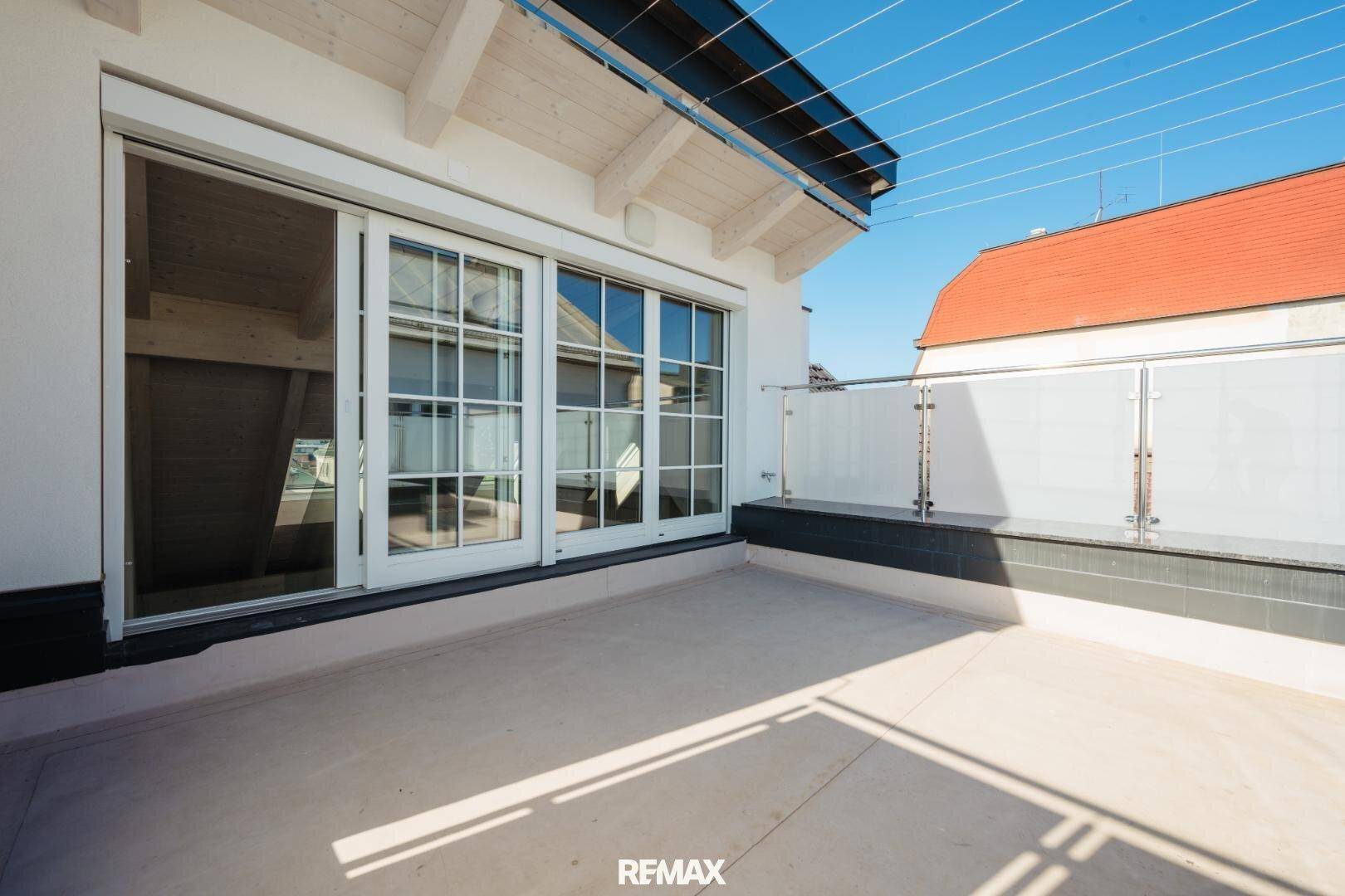 Sonniger Terrassenbereich mit Glasbrüstung und großzügiger Schiebetür zum Innenraum.
