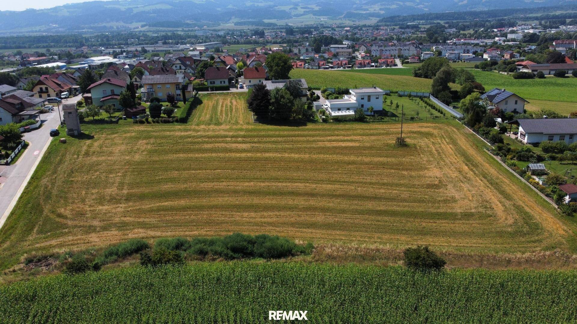 Weitläufiges Feld umgeben von Wohnhäusern und einer malerischen Bergkulisse.