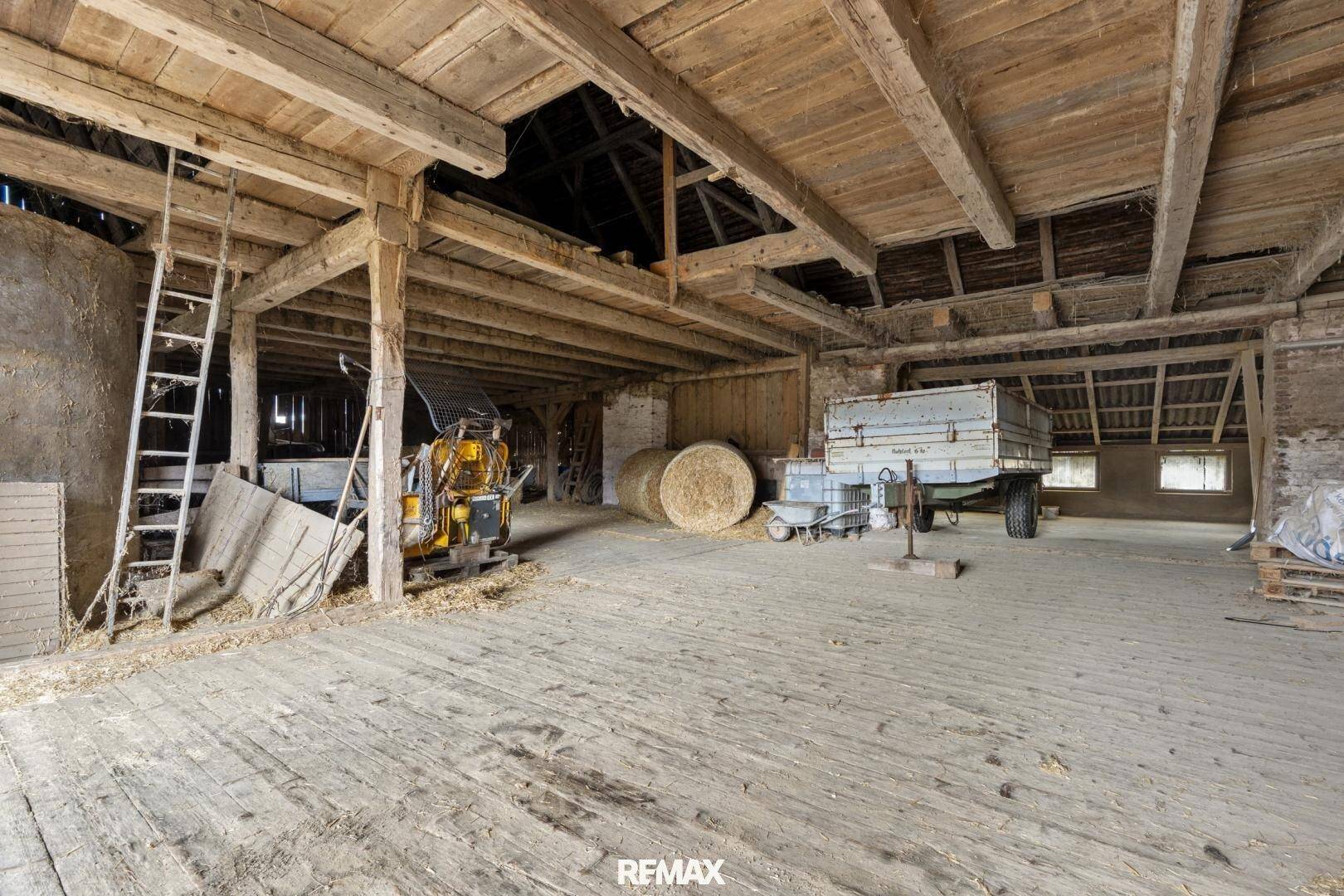 Geräumiger Lagerbereich in einer Scheune mit Holzboden, sichtbaren Balken und landwirtschaftlichen Geräten.
