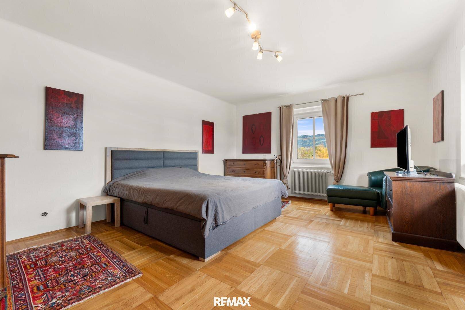 Helles Schlafzimmer mit Parkettboden, großem Bett und Blick auf die Landschaft.
