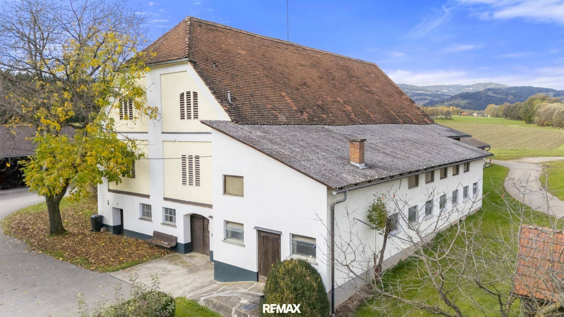 Großes landwirtschaftliches Gebäude mit traditioneller Architektur und rotem Ziegeldach in ländlicher Umgebung.