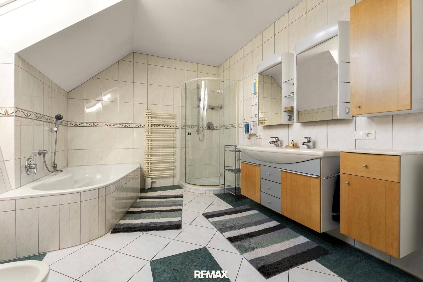 Badezimmer mit Badewanne, Duschkabine, Doppelwaschbecken und Fliesen an Wänden und Boden.