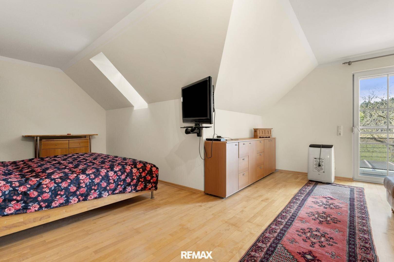 Schlafzimmer im Dachgeschoss mit Holzboden, Dachschrägen und Zugang zu einem Balkon.