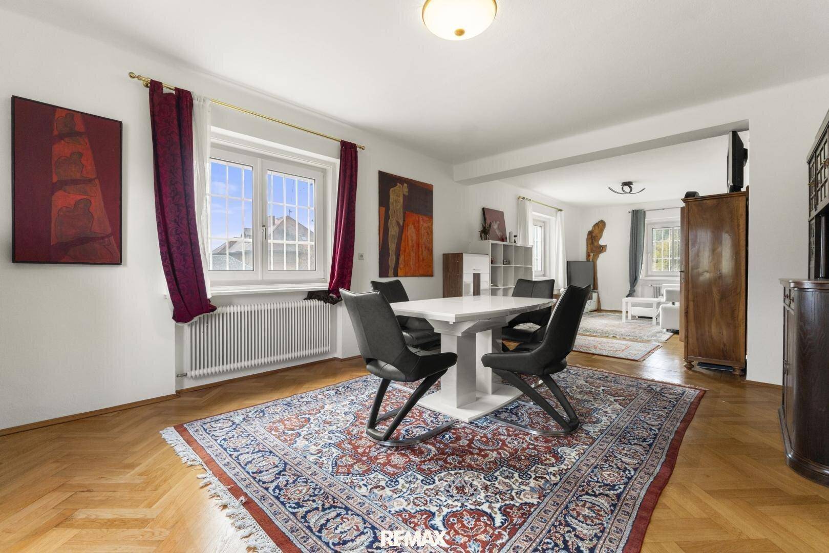 Eleganter Essbereich mit weißem Tisch, schwarzen Stühlen und einem großen Teppich auf Fischgrätparkett.